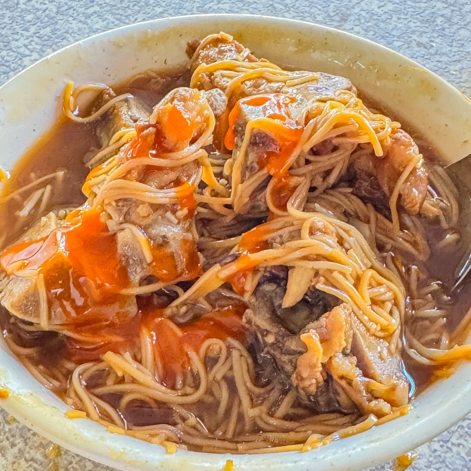 手工麵線細節俯拍，勾芡湯汁裹附麵身，佐以蒜泥和香菜點綴