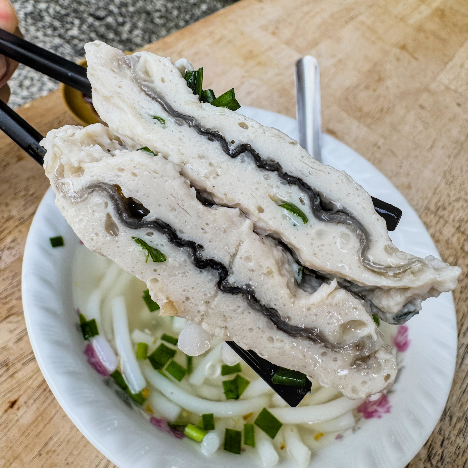 扁扁的魚皮丸特寫，強調其外層Q彈內餡包裹魚皮膠質的獨特口感，為綜合米粉湯的精華。