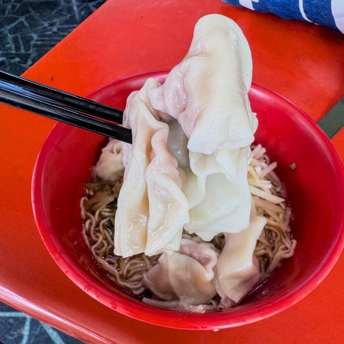 使用筷子夾起廣招英巨大的溫州餛飩，外皮滑嫩且內餡紮實鮮甜