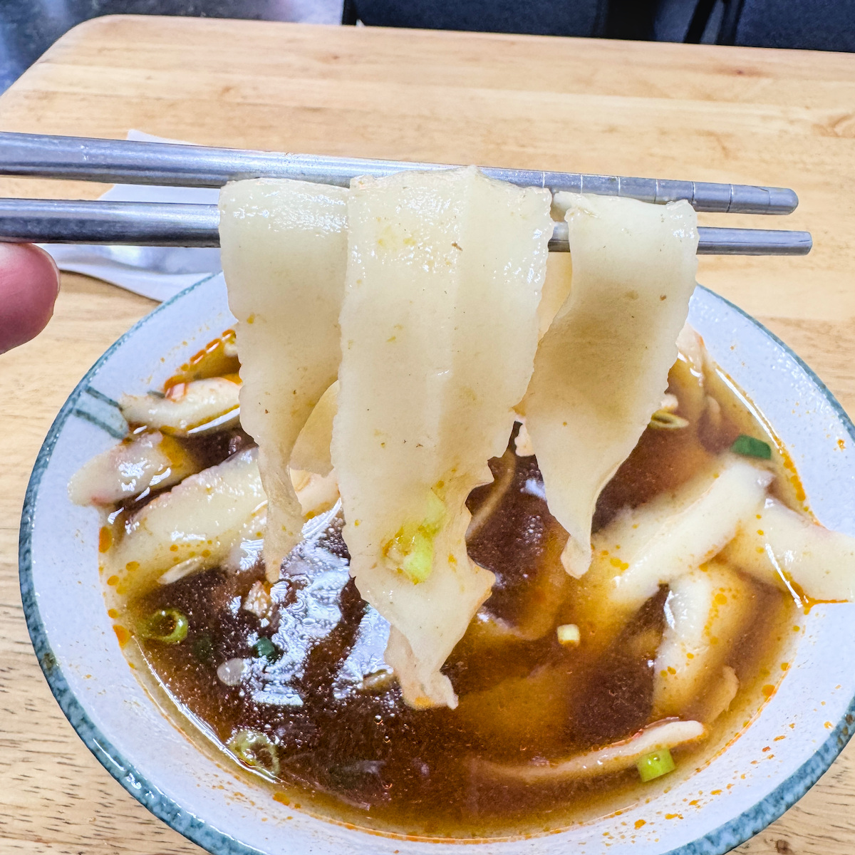 筷子夾起吸附滿滿紅燒湯汁的刀削麵條，厚實的麵體展現出絕佳的彈性與紮實口感