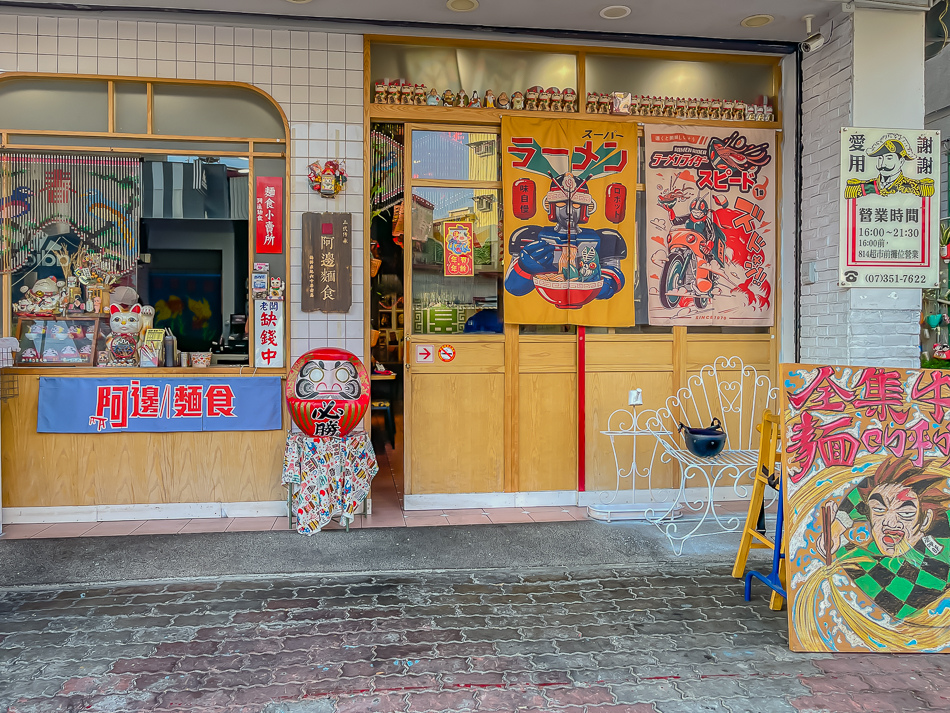 店門口與炭呷郎插畫|高雄楠梓美食 阿邊麵食 店門口與炭呷郎插畫,高雄市楠梓區阿邊麵食實景,鄰近楠梓火車站的60年老店,提供陽春麵、牛肉乾拌麵、魚丸湯、滷味與各式小菜,店內充滿日式收藏與溫馨用餐空間,是楠梓美食、高雄小吃推薦。